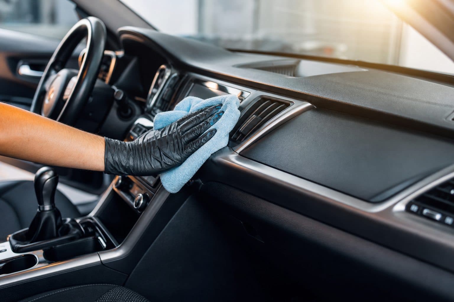 Gloved hand wiping a car dashboard with a microfiber cloth during interior detailing