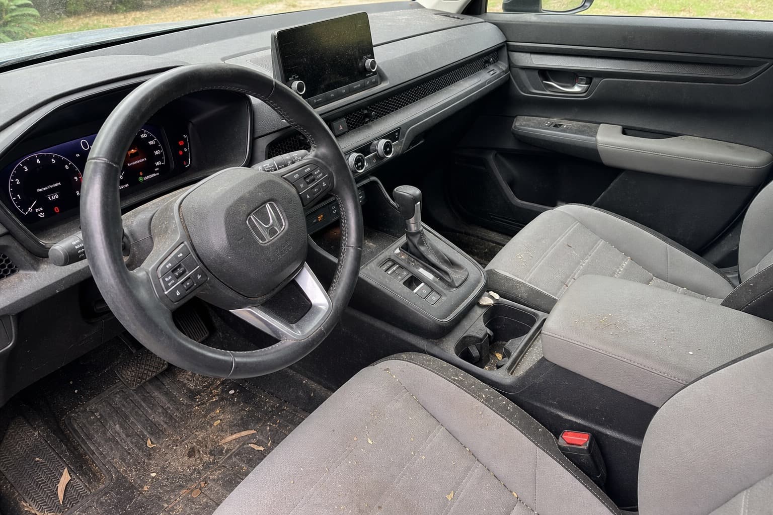 Modern SUV interior before detailing — dusty touchscreen, crumbs on gray seats, debris on floor mats